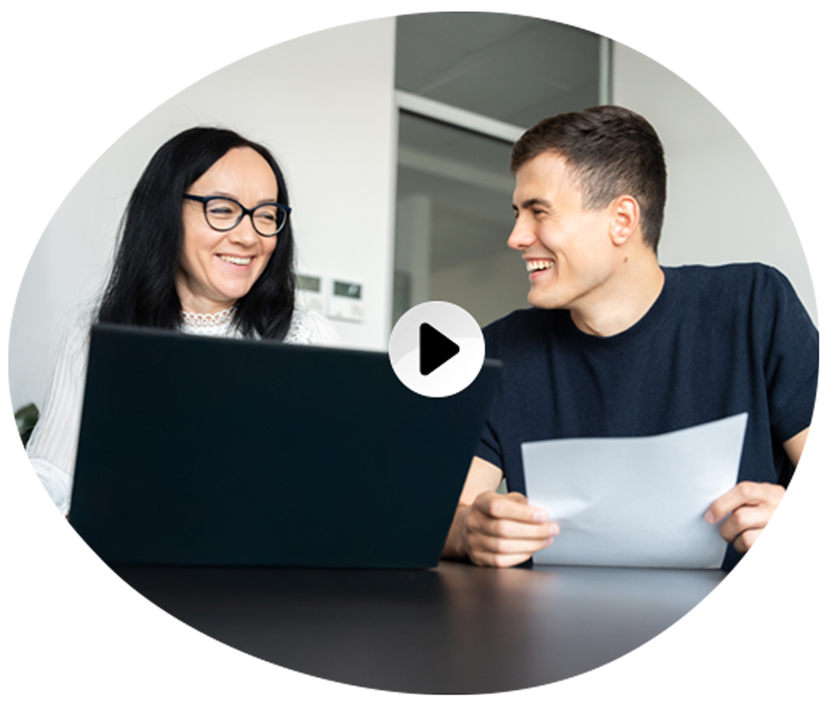 A woman and a man are sitting at a table, smiling. The woman is working on a laptop, while the man is holding a piece of paper. A play button icon is overlaid on the image, suggesting it is a video thumbnail.