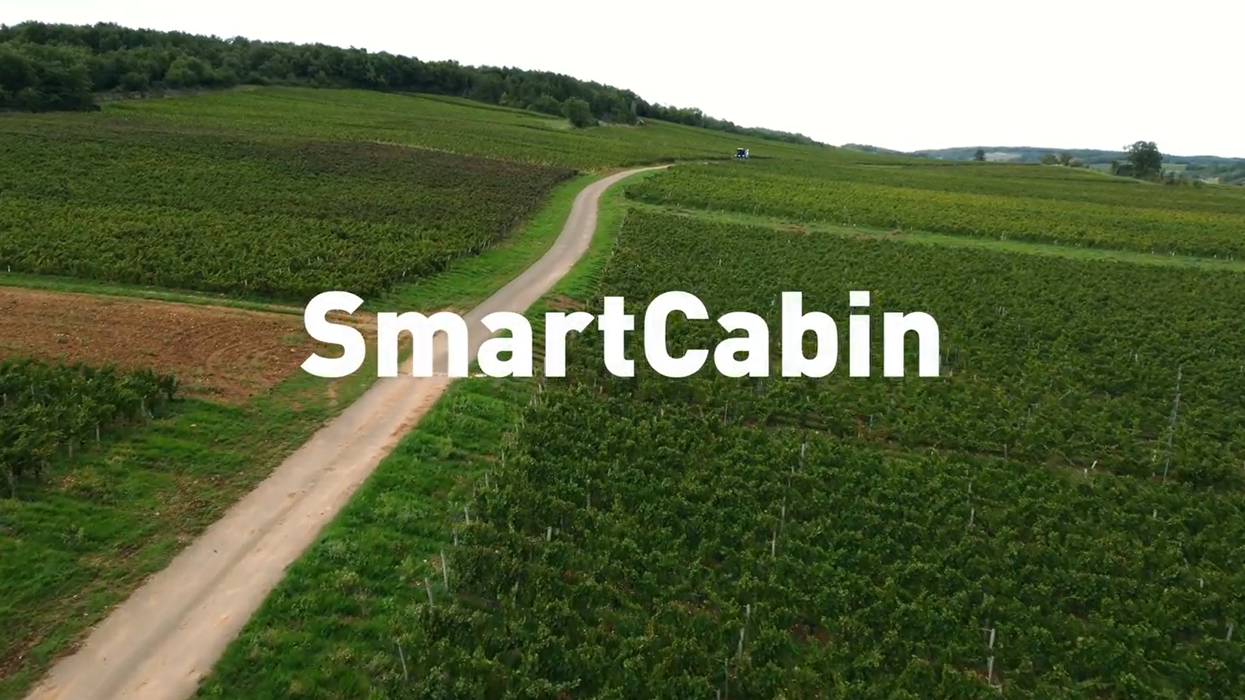 A dirt road winds through green fields and vineyards under a clear sky, with the word "SmartCabin" prominently displayed in white text across the center of the image.
