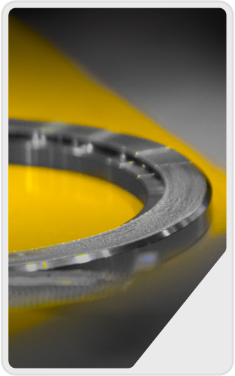 Close-up of a metallic circular object on a reflective surface, with a yellow and gray background, creating an abstract and modern composition.